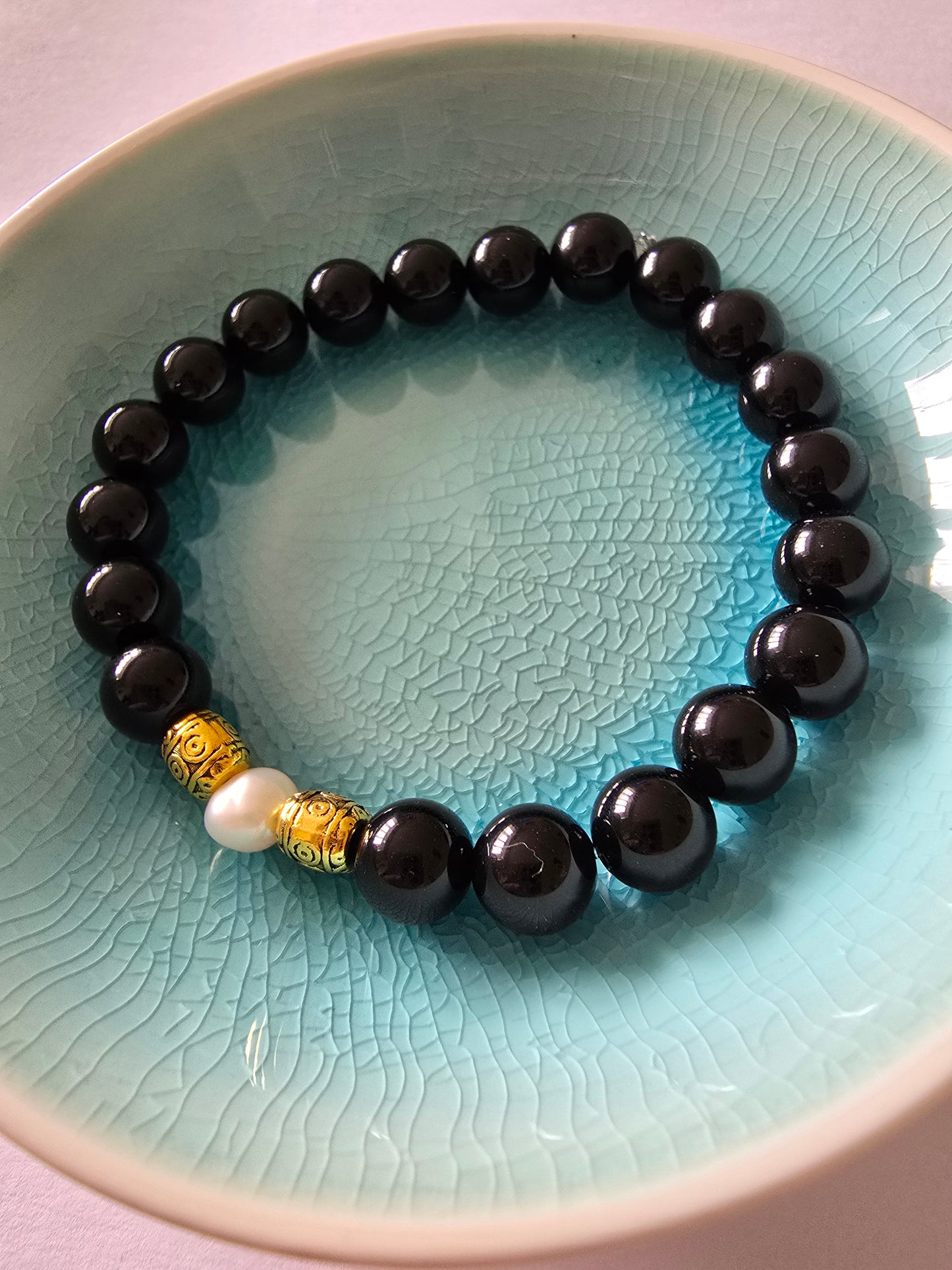Black beaded bracelet with a gold and pearl accent on a textured blue plate.