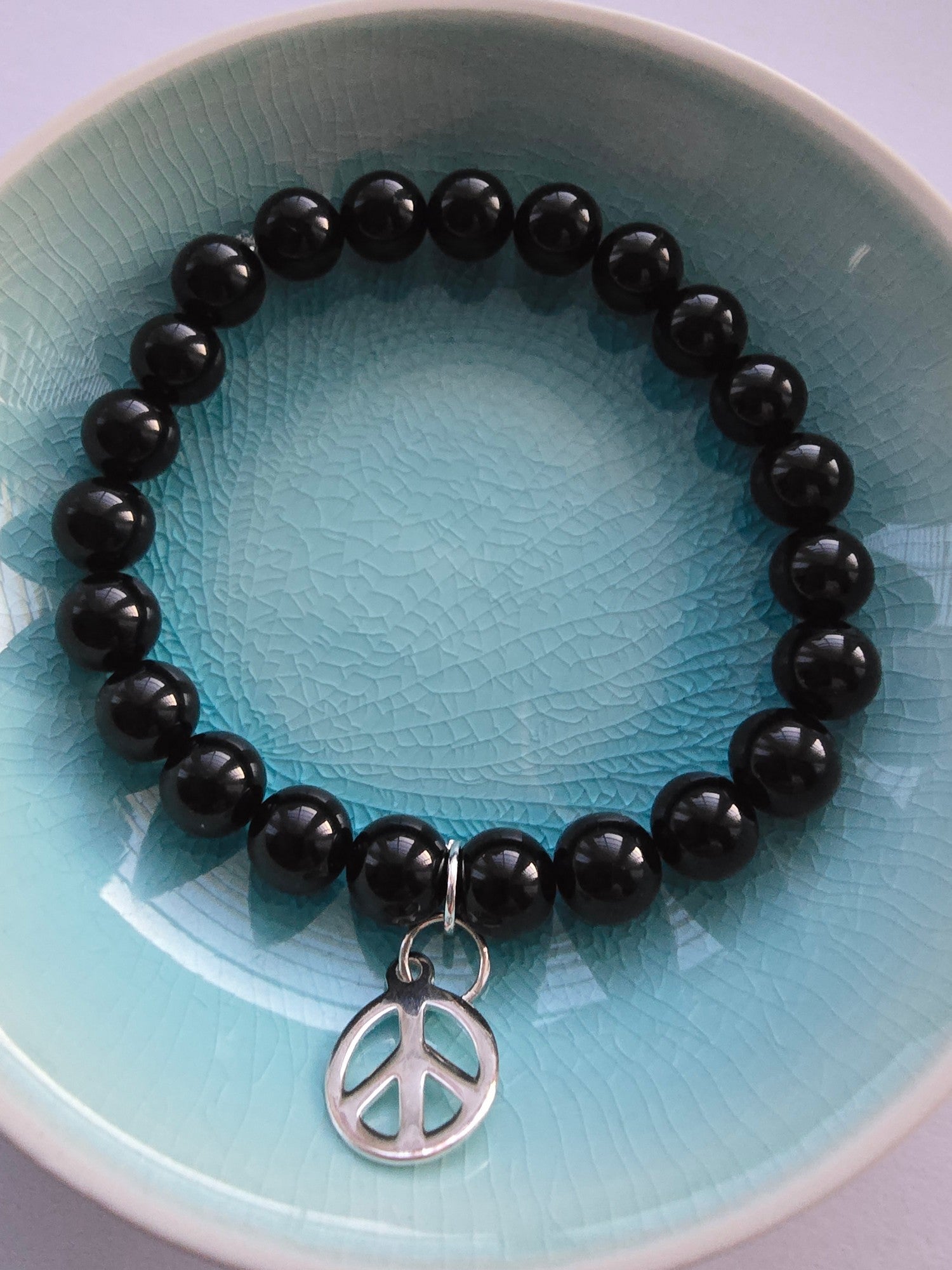 Black beaded bracelet with a peace sign charm on a blue plate