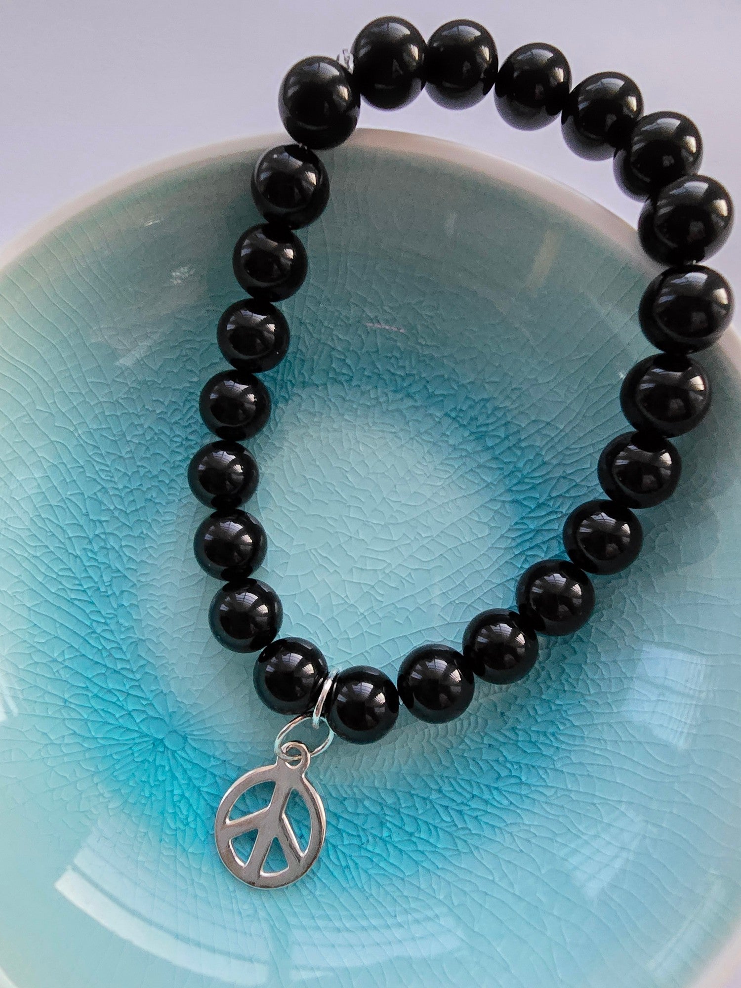 Black beaded bracelet with a peace symbol charm on a light blue background