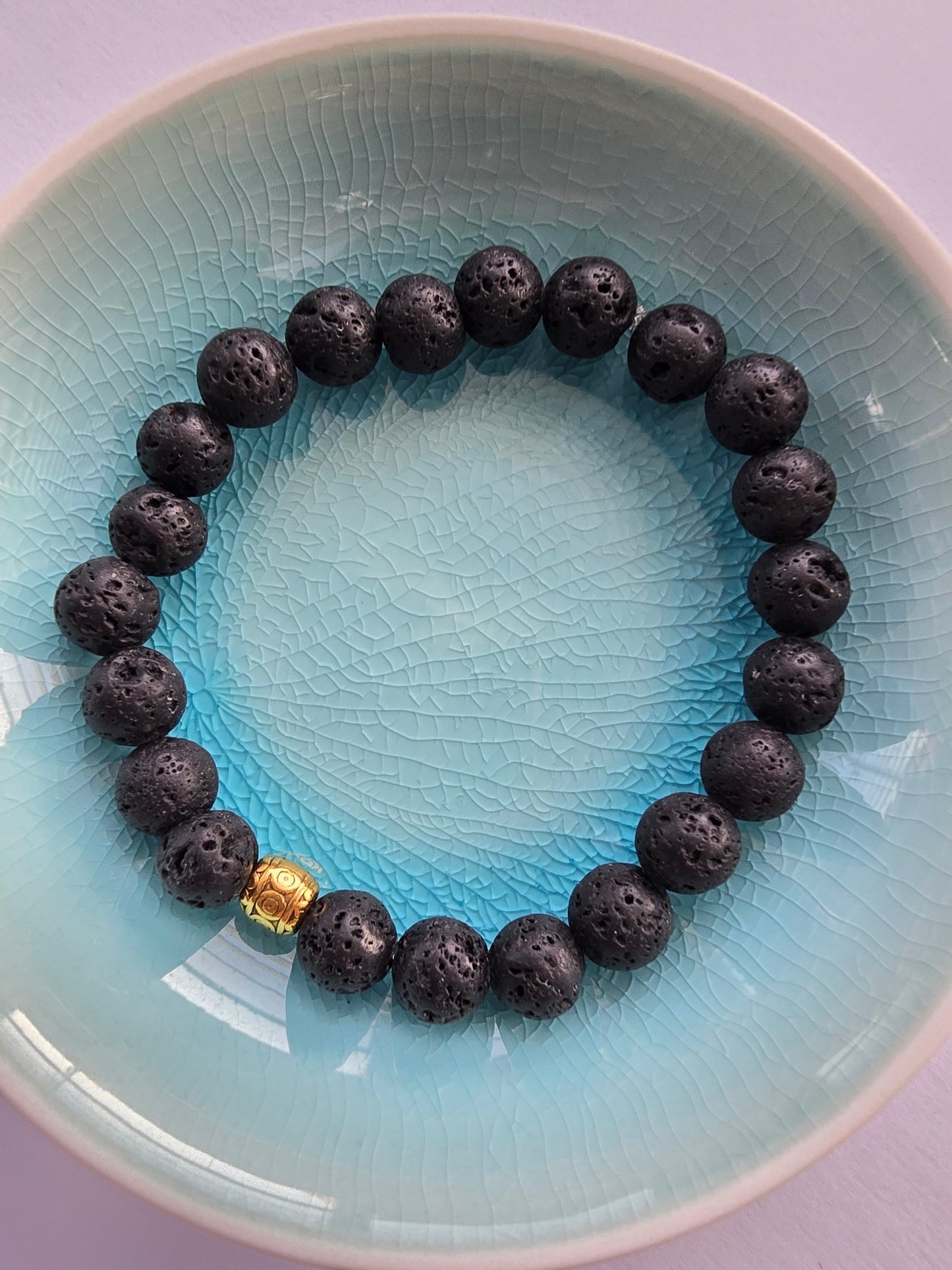 Black lava stone beaded bracelet with a gold clasp on a light blue plate