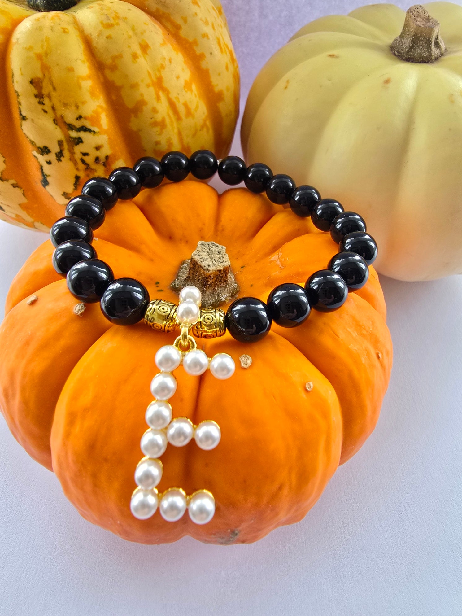 Black agate beaded bracelet with pearl letter E and gold beads on an orange pumpkin