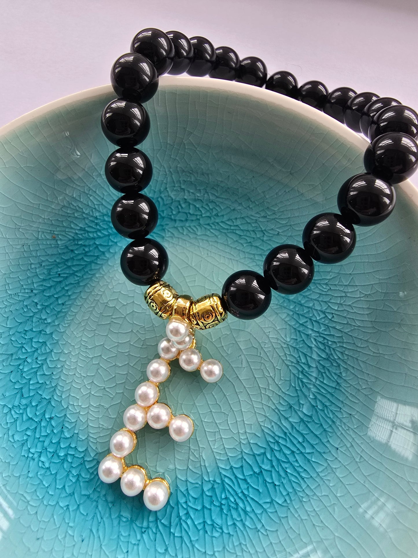 Black beaded agate bracelet with a pearl dangly letter E and gold patterned beads