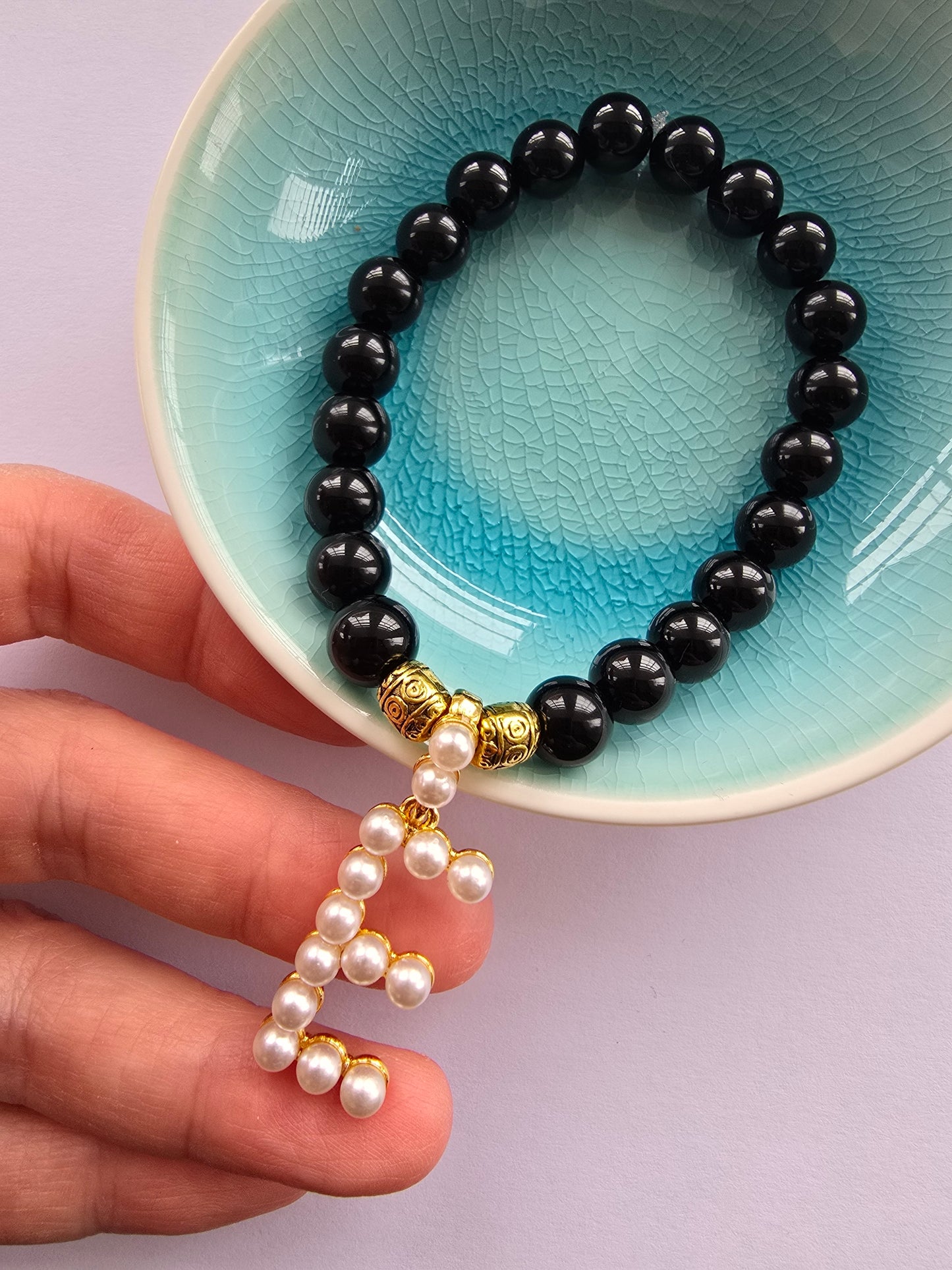 Black beaded agate bracelet with a pearl dangly letter E and gold patterned beads