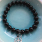 Black beaded bracelet with a peace sign charm on a blue plate