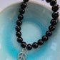 Black beaded bracelet with a peace symbol charm on a light blue background