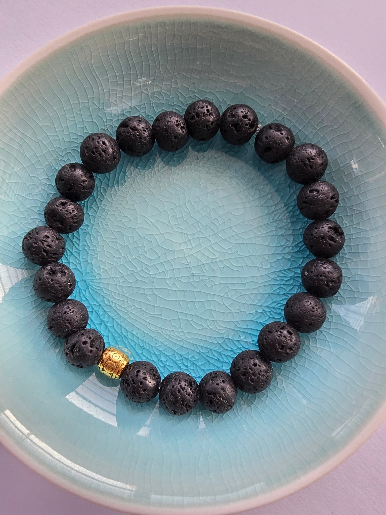 Black lava stone beaded bracelet with a gold clasp on a light blue plate