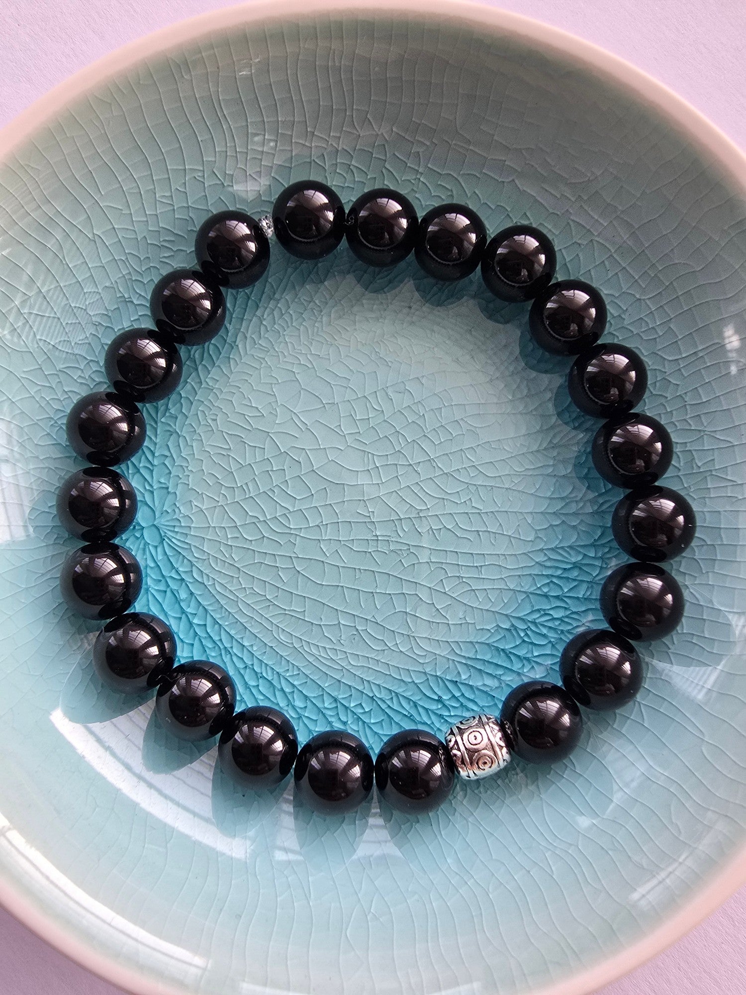 Black beaded bracelet with a silver tibetan bead clasp on a light blue ceramic plate