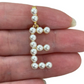 Pearl letter 'E' pendant held between fingers on a white background