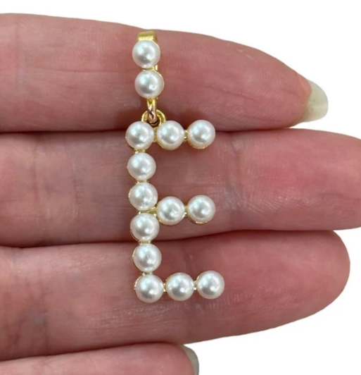 Pearl letter 'E' pendant held between fingers on a white background