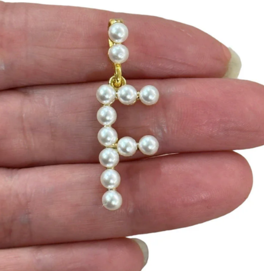 Pearl letter 'F' pendant held between fingers on a white background