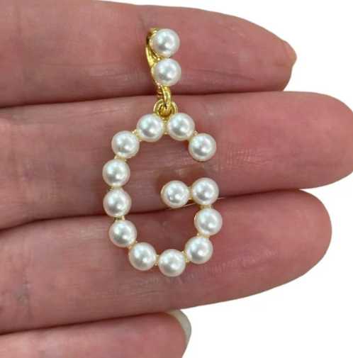 Pearl letter G held between fingers against a neutral background