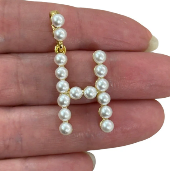 Pearl letter 'H' charm held between fingers against a white background