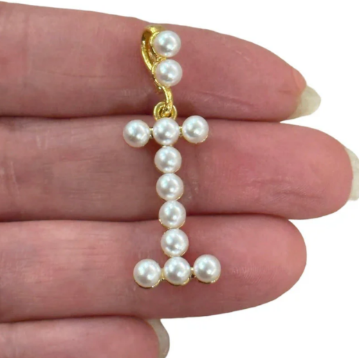 Pearl capital letter I held between fingers on a white background