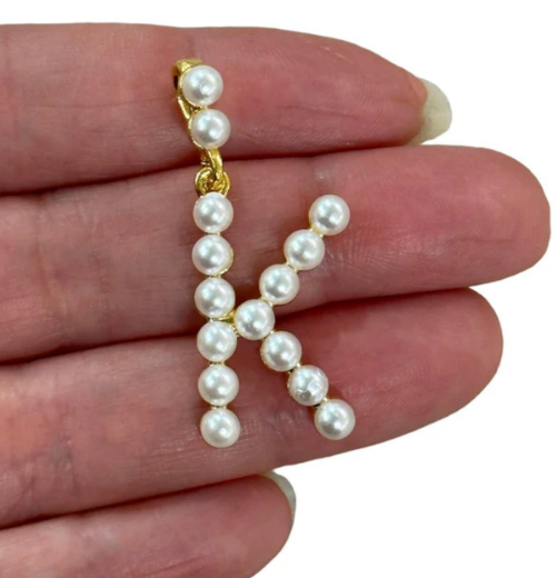 Pearl letter K on a hand with a plain background