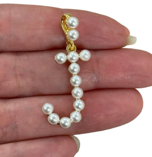 Pearl capital letter J held between fingers on a white background