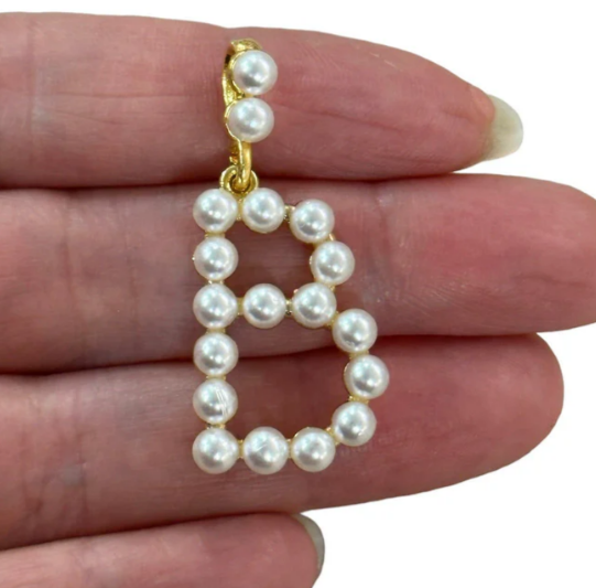 Pearl letter 'B' charm held between fingers on a white background