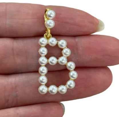 Pearl letter 'B' charm held between fingers on a white background