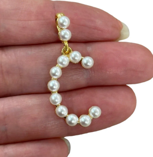 Pearl letter C held between fingers on a white background