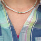 A close-up of a person wearing a white iridescent beaded necklace over a blue and green plaid shirt.