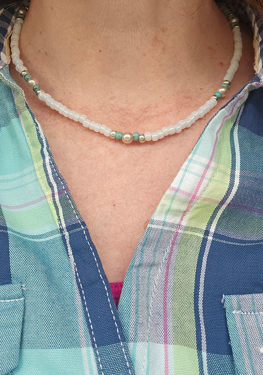 A close-up of a person wearing a white iridescent beaded necklace over a blue and green plaid shirt.